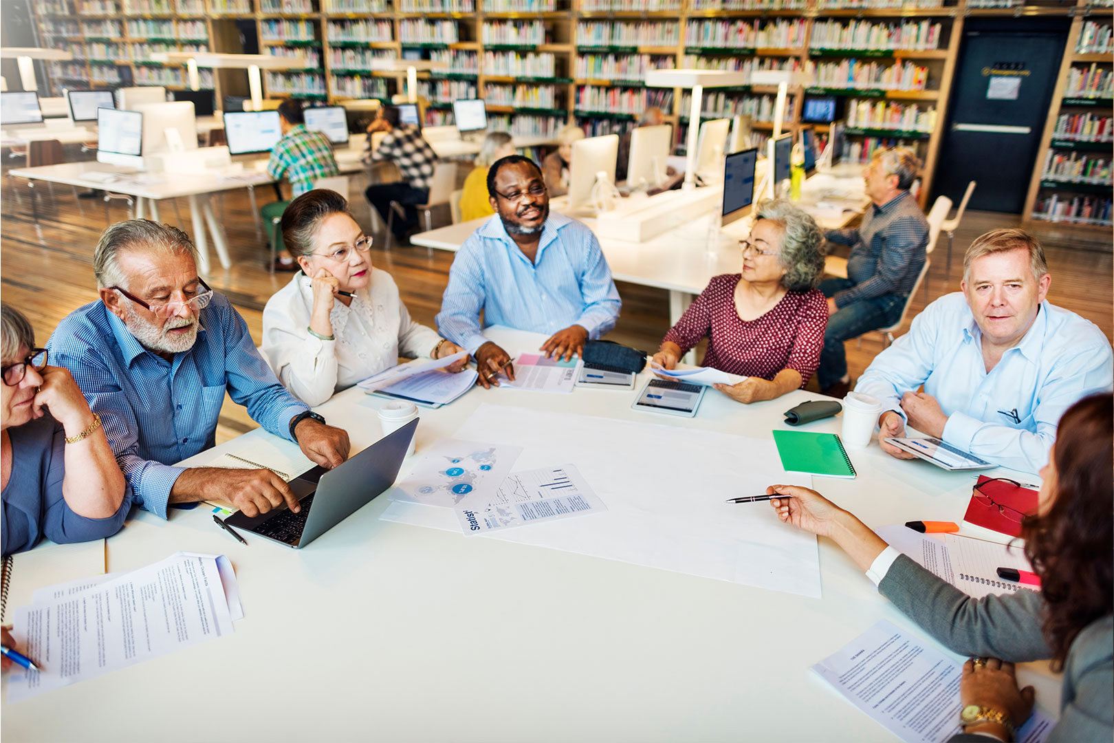 7 people with laptops meeting at a large table in a library